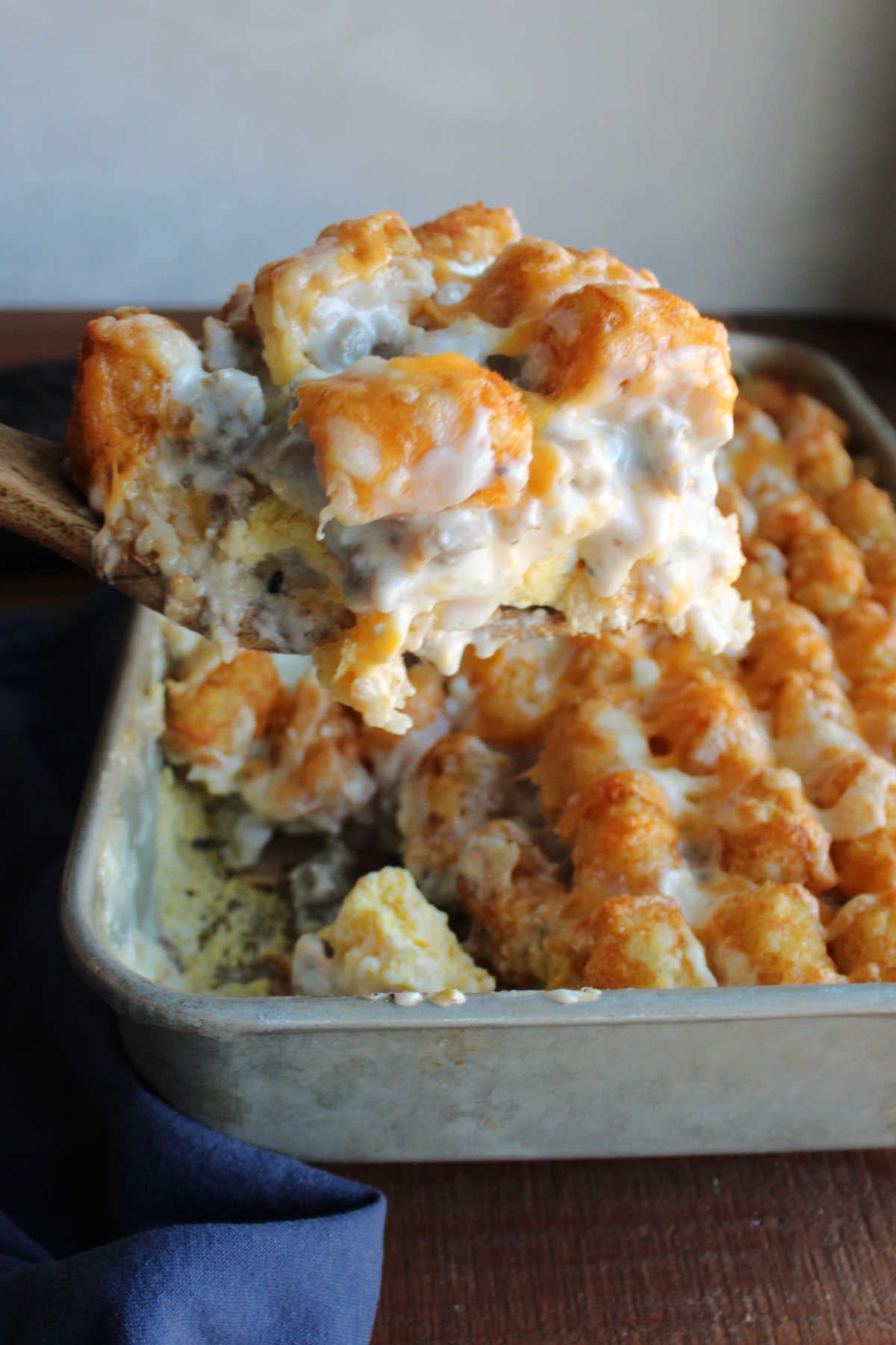 Biscuits and Gravy Tater Tot Casserole 6 Spatula lifting a helping of tater tot casserole out of the pan showing the layers of goodness with creamy sausage gravy bringing it all together.
