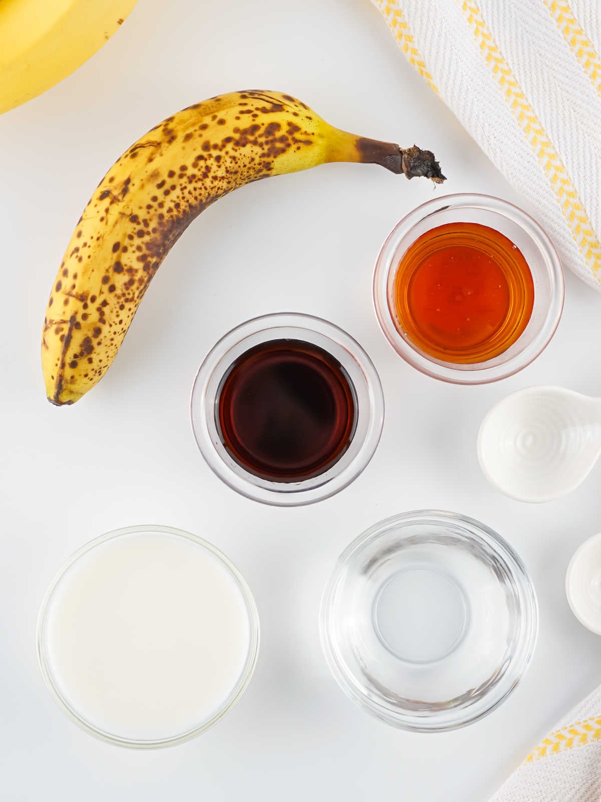 Ingredients including ripe bananas, milk, water, vanilla extract, and maple syrup ready to be made into banana milk. 