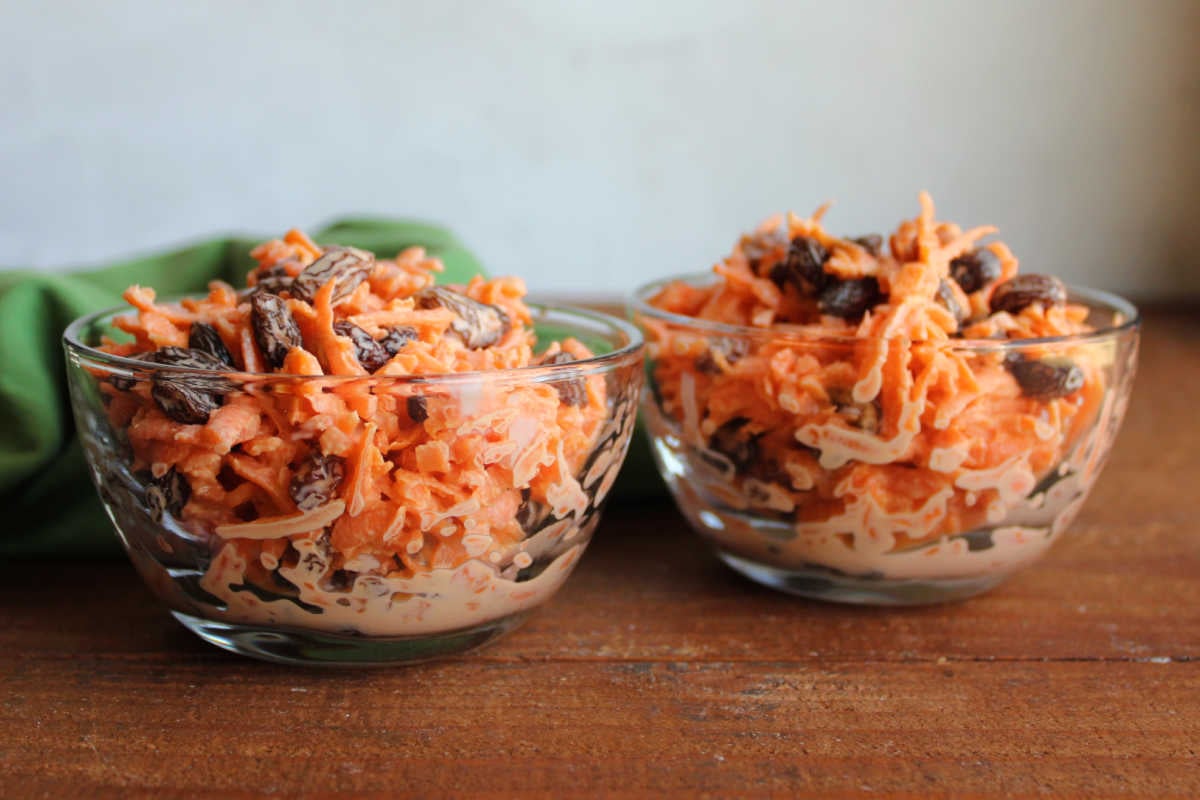 Two small glass bowls filled with servings of carrot raisin salad with creamy Tang dressing. 