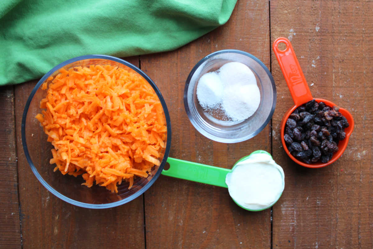 Ingredients including grated carrots, tang powder, raisins, and mayonnaise ready to be made into carrot salad. 