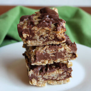 No bake oatmeal cookie bars with layers of oat mixture around a chocolate and peanut butter layer stacked on top of each other.