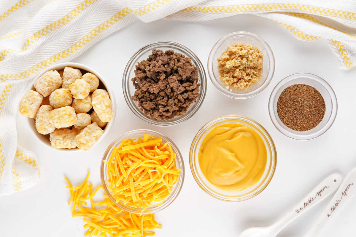 Ingredients including tater tots, ground beef, taco seasoning cheese sauce, shredded cheese and minced onion ready to be made into a crockpot tater tot casserole. 