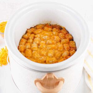 Finished tater tot casserole in slow cooker with golden brown tater tots and melted cheese on top.