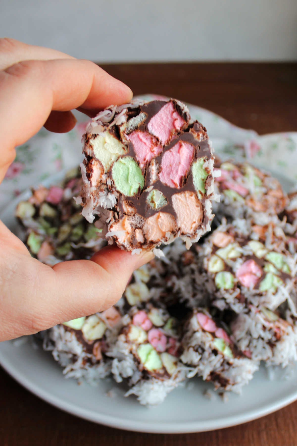 Hand holding a church window cookie showing chocolate holding together the bits of colorful marshmallow with bits of coconut on the outside. 