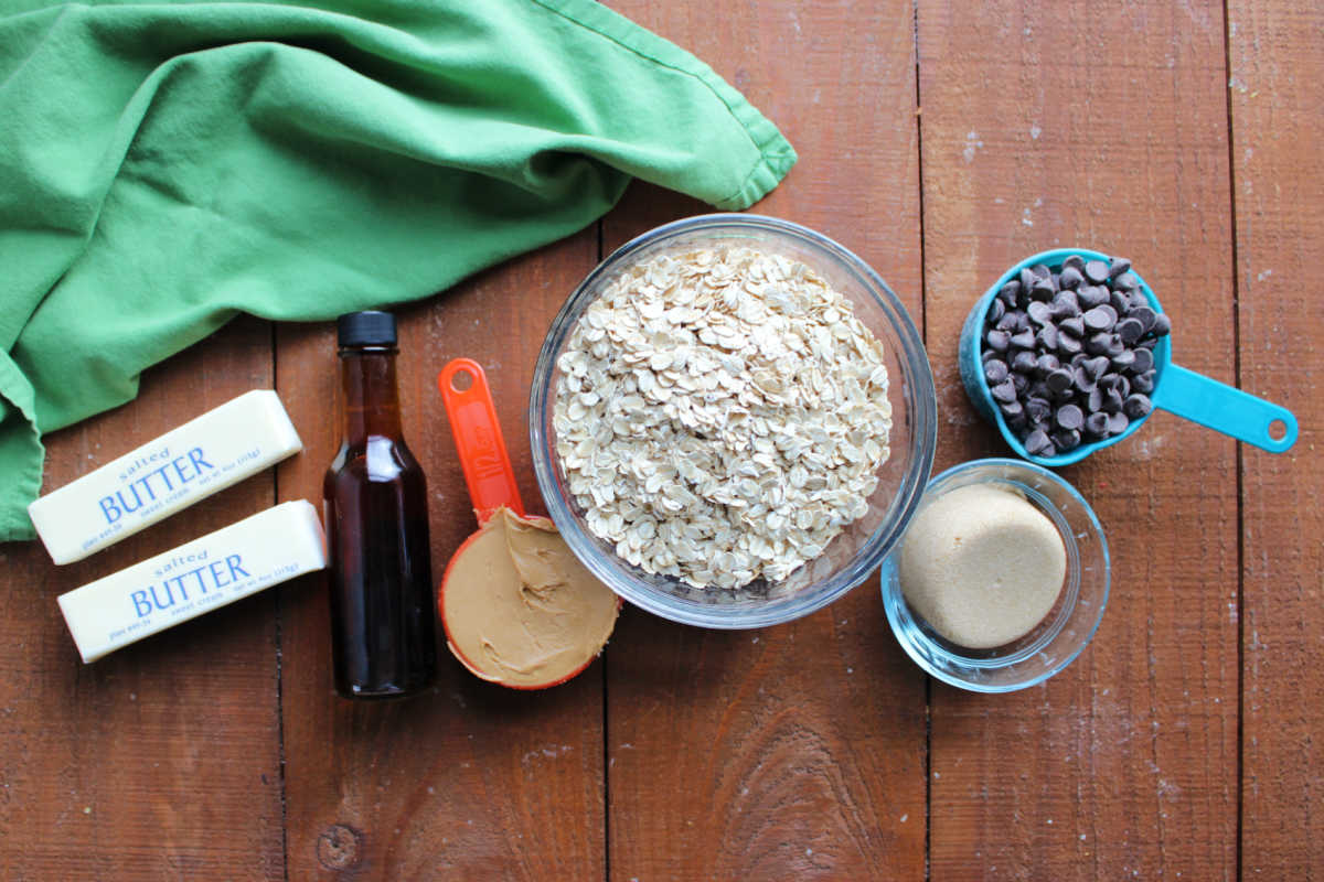 Ingredients including butter, vanilla, peanut butter, oats, brown sugar, and chocolate chips ready to be made into no bake cookie bars. 