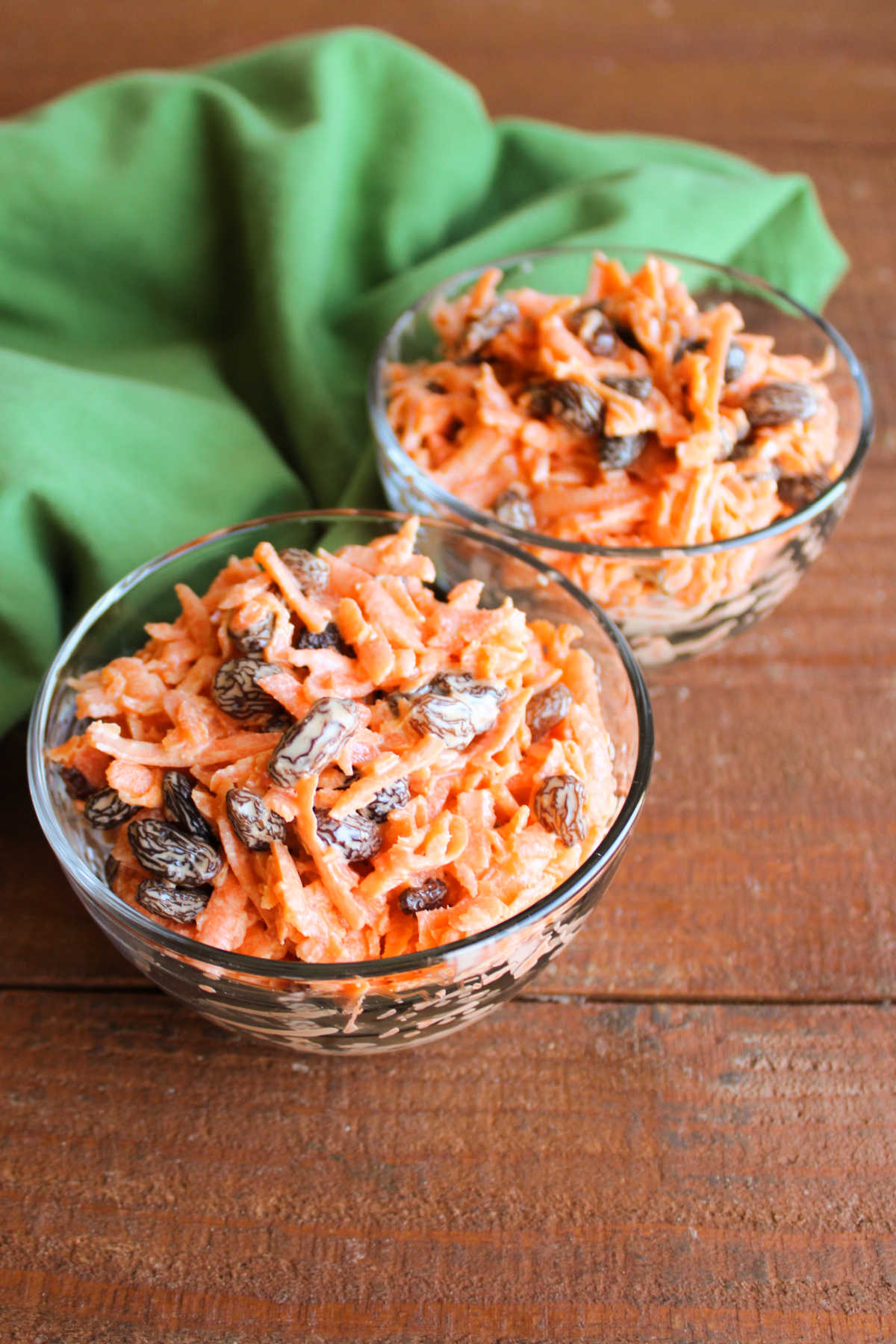 Looking down on bowls of carrot salad showing bits of shredded carrots and raisins in dressing. 
