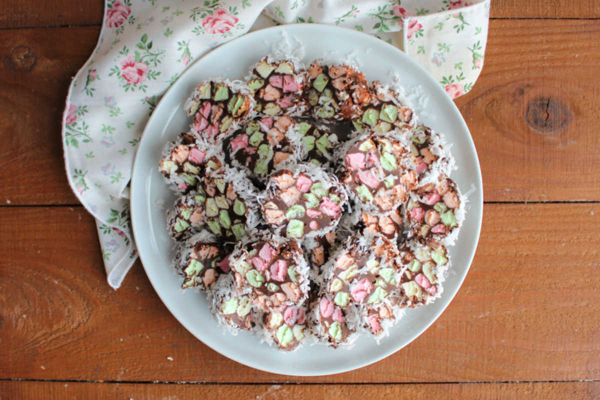 White platter piled with no bake stained glass candy with colorful marshmallow bits in chocolate with coconut around the edges. 