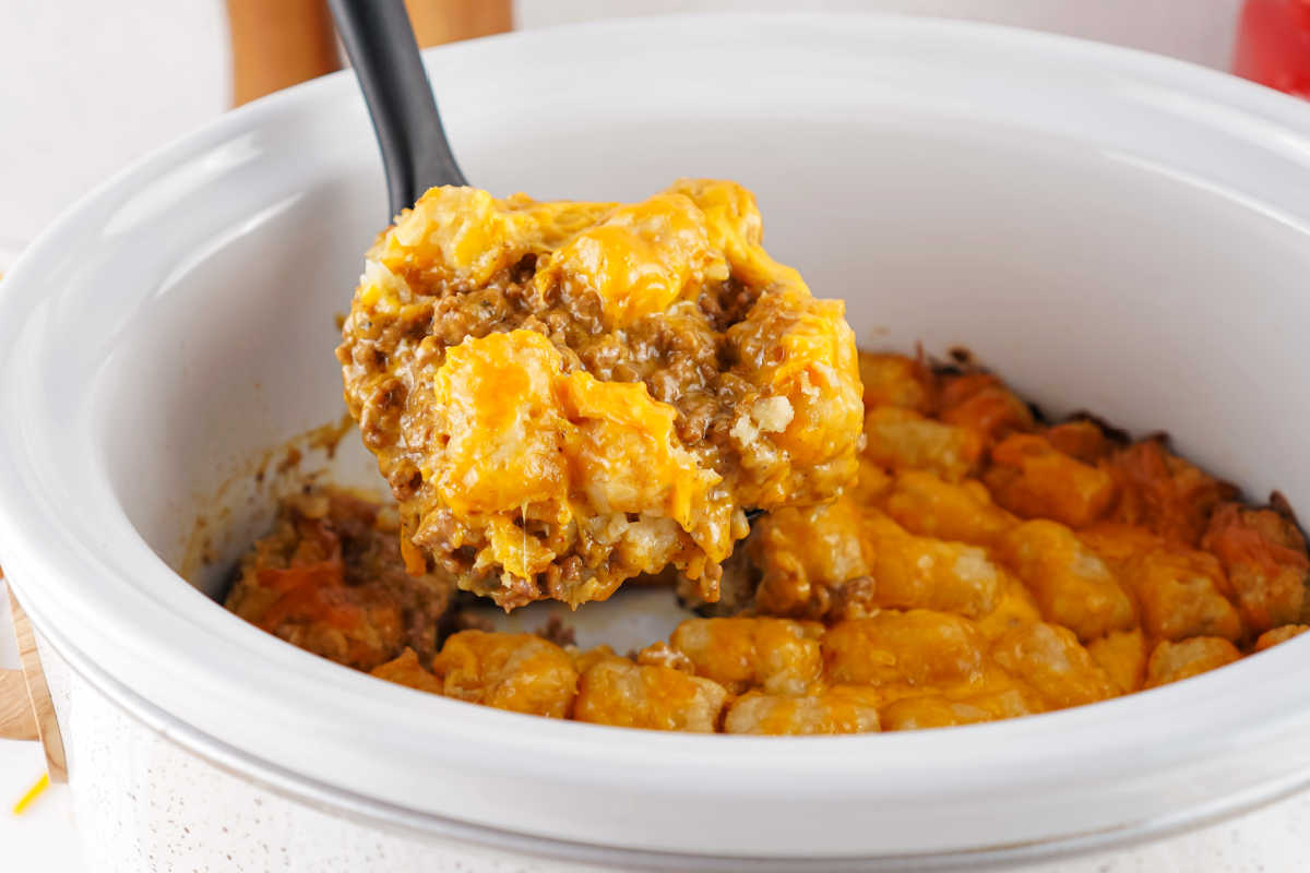 Serving spoon getting a scoop of taco tater tot casserole out of a slow cooker. 