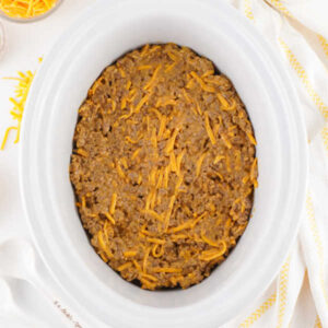 Meat and cheese mixture spread over the top of some tater tots in a slow cooker.