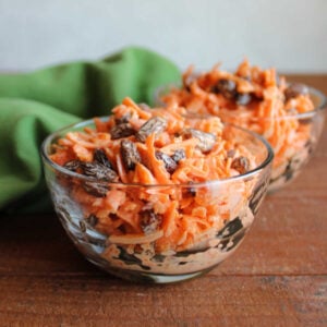 Two small bowl filled with salad made from shredded carrots and raisins in a light coating of creamy orange dressing.
