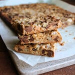 Three chippy dippy squares stacked on top of each other showing how the layers of graham cracker crumbs, coconut, chocolate chips, pecans, and butterscotch chips have all come together and the caramelized condensed milk is holding them together.
