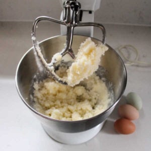 Stand mixer with creamed butter and sugar mixture inside with 3 eggs nearby.
