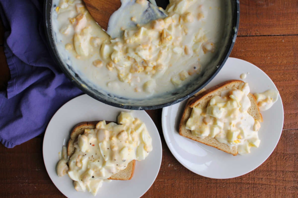 Skillet filled with creamed eggs next to two plates of toast topped with creamy egg gravy. 