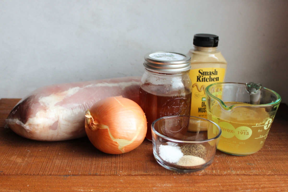 Ingredients including a pork loin roast, onion, honey, Dijon mustard, salt, pepper, garlic powder, and chicken broth ready to be made into slow cooker honey mustard pork roast. 