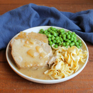 Dinner plate with pork loin slices smothered in honey mustard and onion gravy served with wide egg noodles and peas.