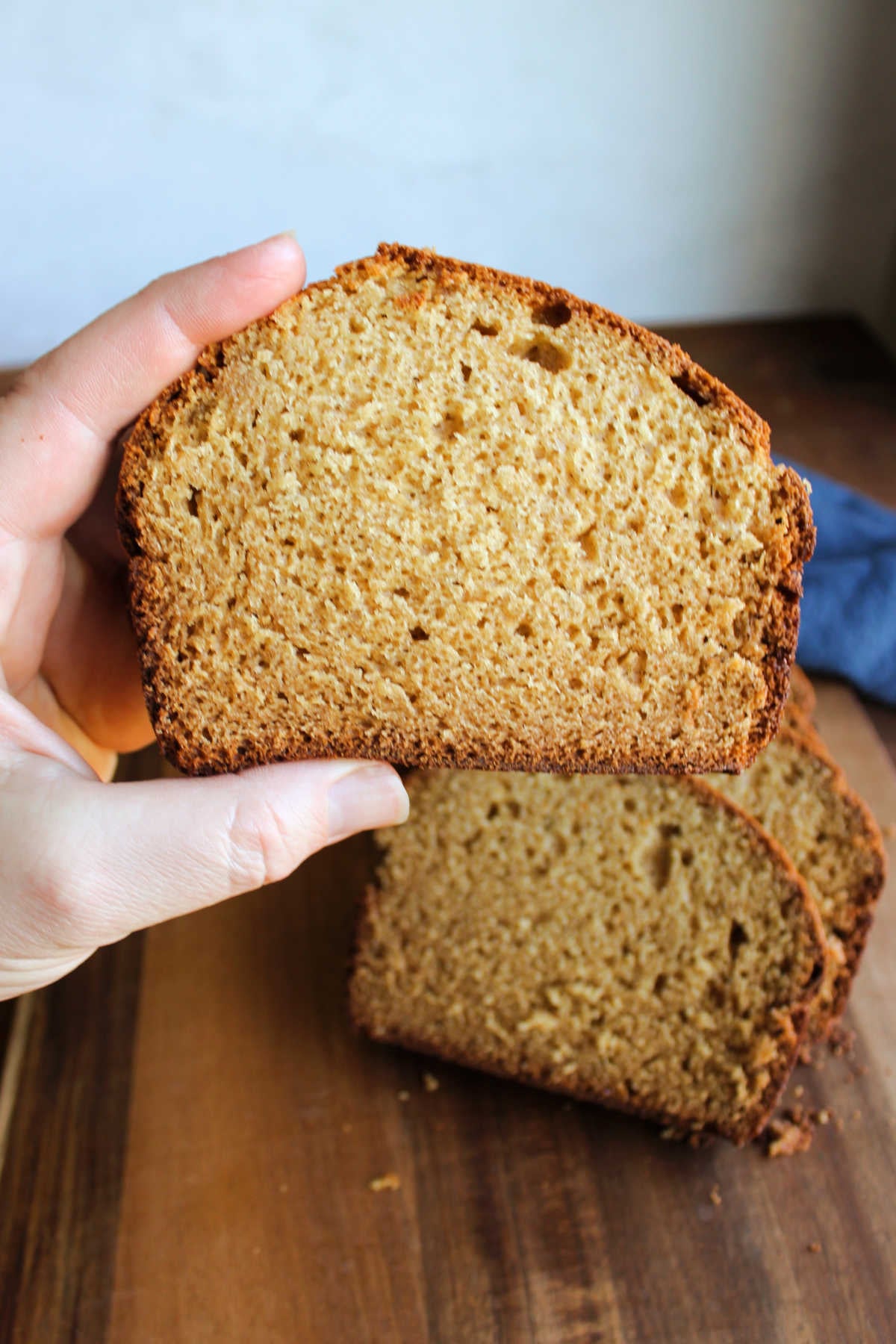 Hand holding a slice of homemade peanut butter bread, showing the interior crumb that is reminiscent of a cake crumb. 