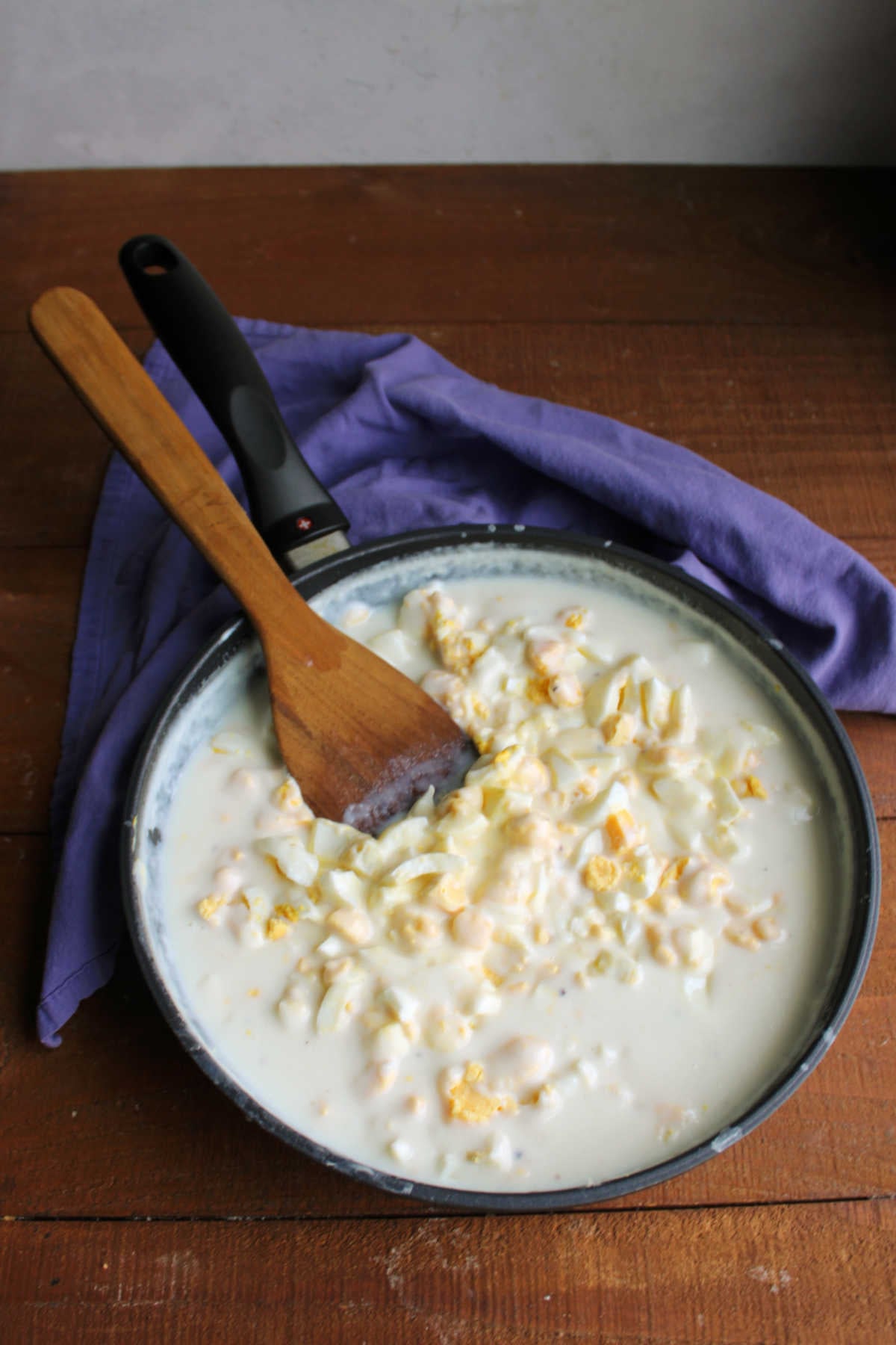 Skillet filled with bechamel sauce and chunks of eggs ready to be served over toast. 