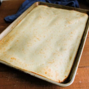 Partially baked pizza crust in sheet pan, ready for toppings.