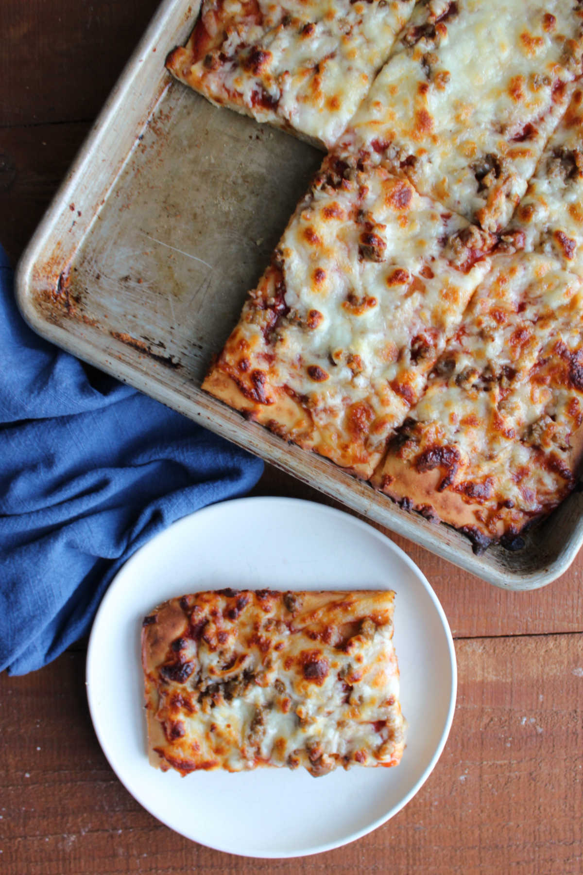 Looking down on a piece of school cafeteria style pizza with more pizza nearby. 
