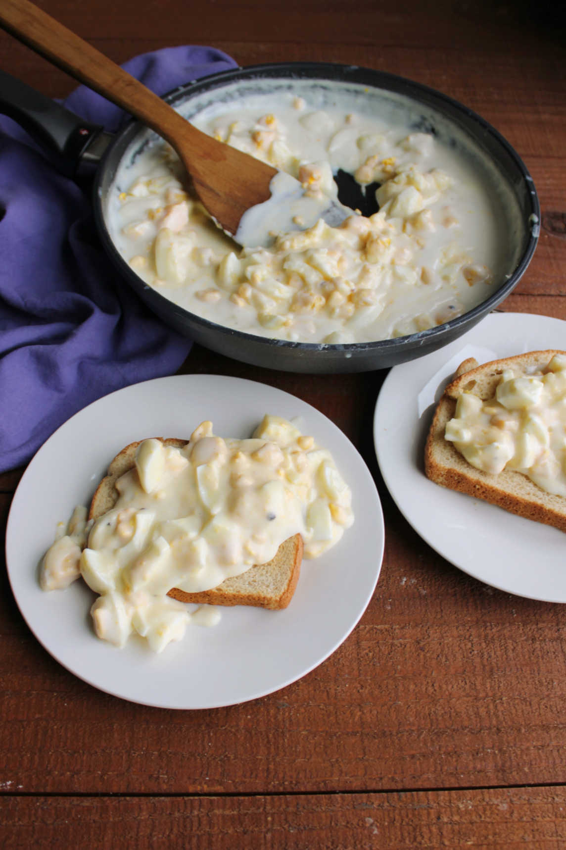 Two plates of egg gravy served over toast next to a skillet with more creamed eggs inside. 