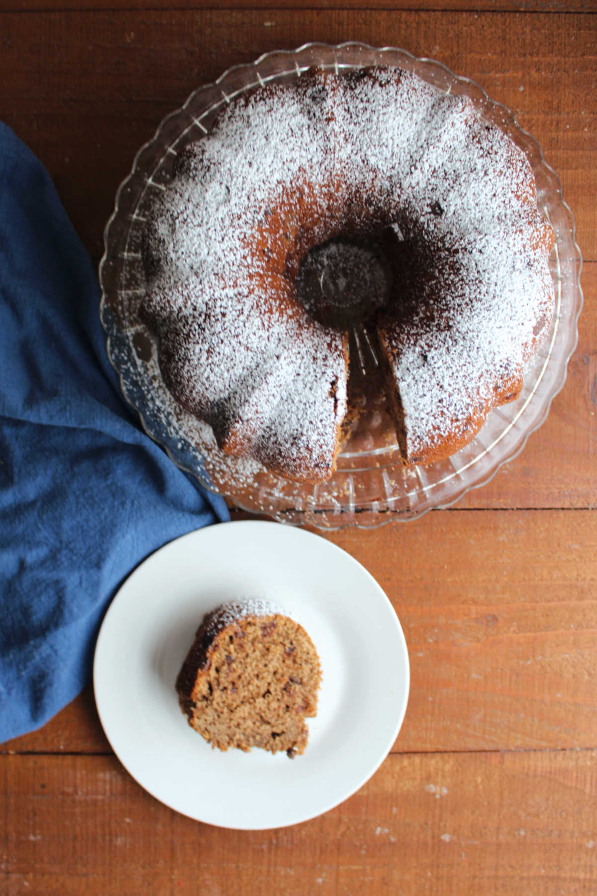 Looking down on a plate with a slice of sourdough mocha nut bread with the rest of the powder sugar dusted circular loaf nearby. 