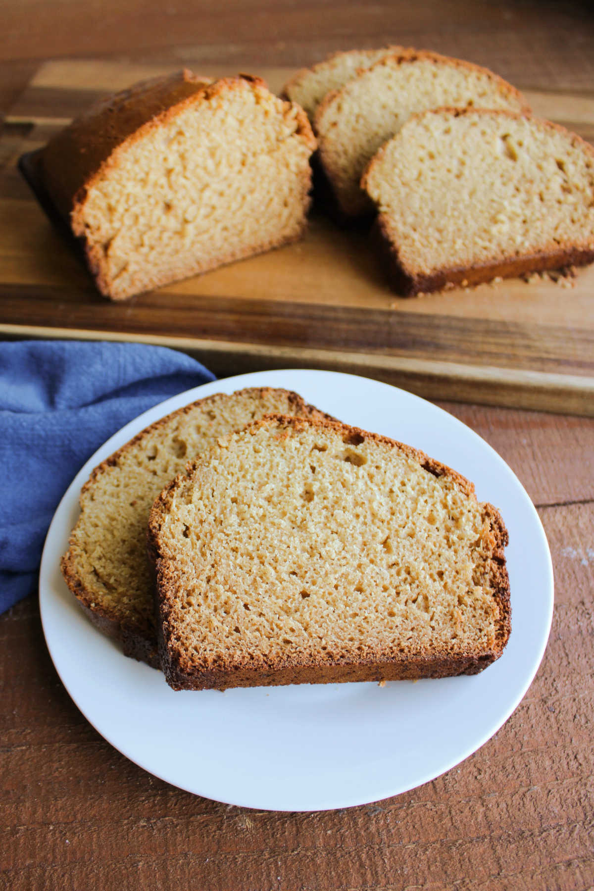 Two slices of peanut butter bread on small plate, ready to eat, with more peanut butter bread on cutting board in the background. 