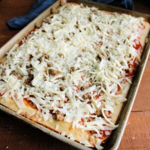Pizza crust topped with sauce, cheese, and sausage, ready to go back in the oven.