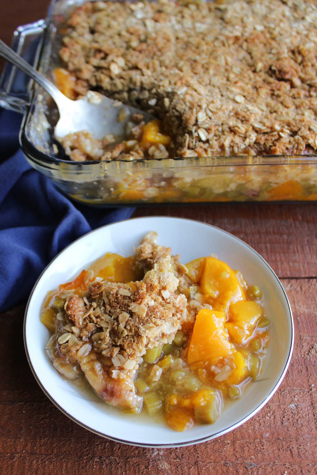 Scoop of peach rhubarb crisp in a small bowl, ready for a scoop of ice cream or dollop of whipped cream. 