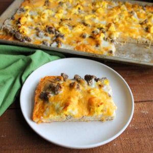Rectangular piece of breakfast pizza with a moderately thick crust topped with creamy sausage gravy, scrambled eggs, and cheese, ready to eat.