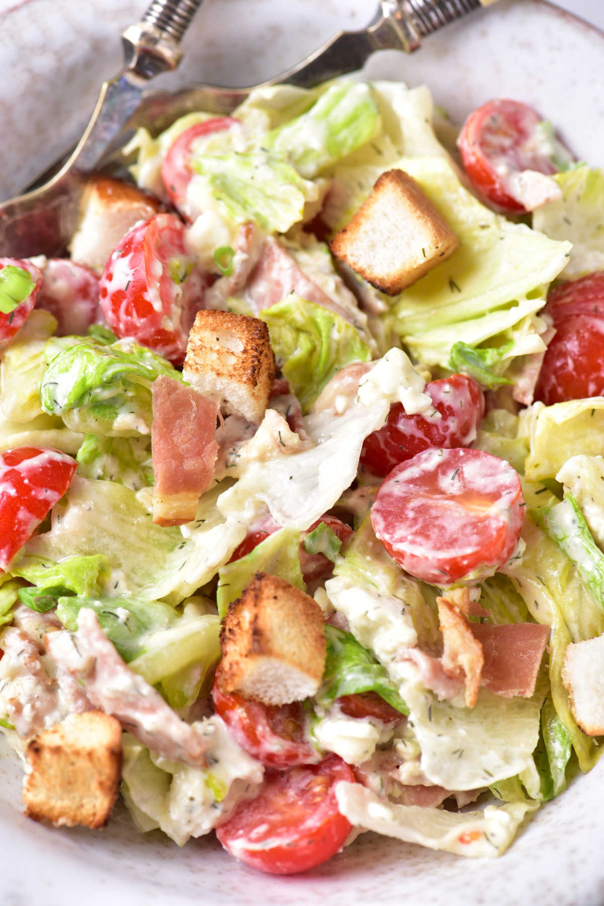 Close up of dressed blt salad showing lettuce, tomatoes, bacon, croutons, and cheese coated creamy dressing. 