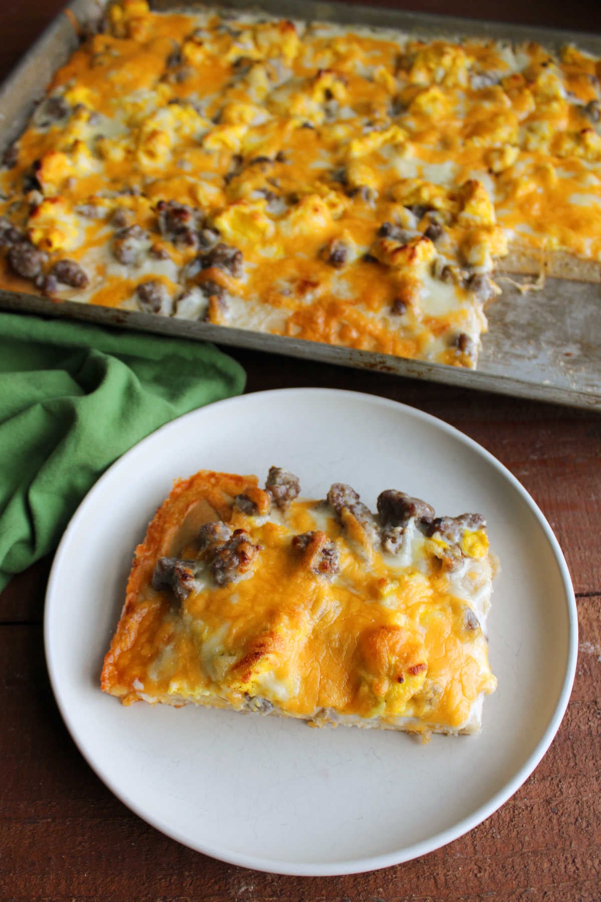 Slice of breakfast pizza on plate next to sheet pan with the rest of the pizza inside. 