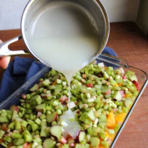 Pouring the thickened sugar mixture out of the saucepan into the baking dish with chopped peaches and sliced rhubarb.