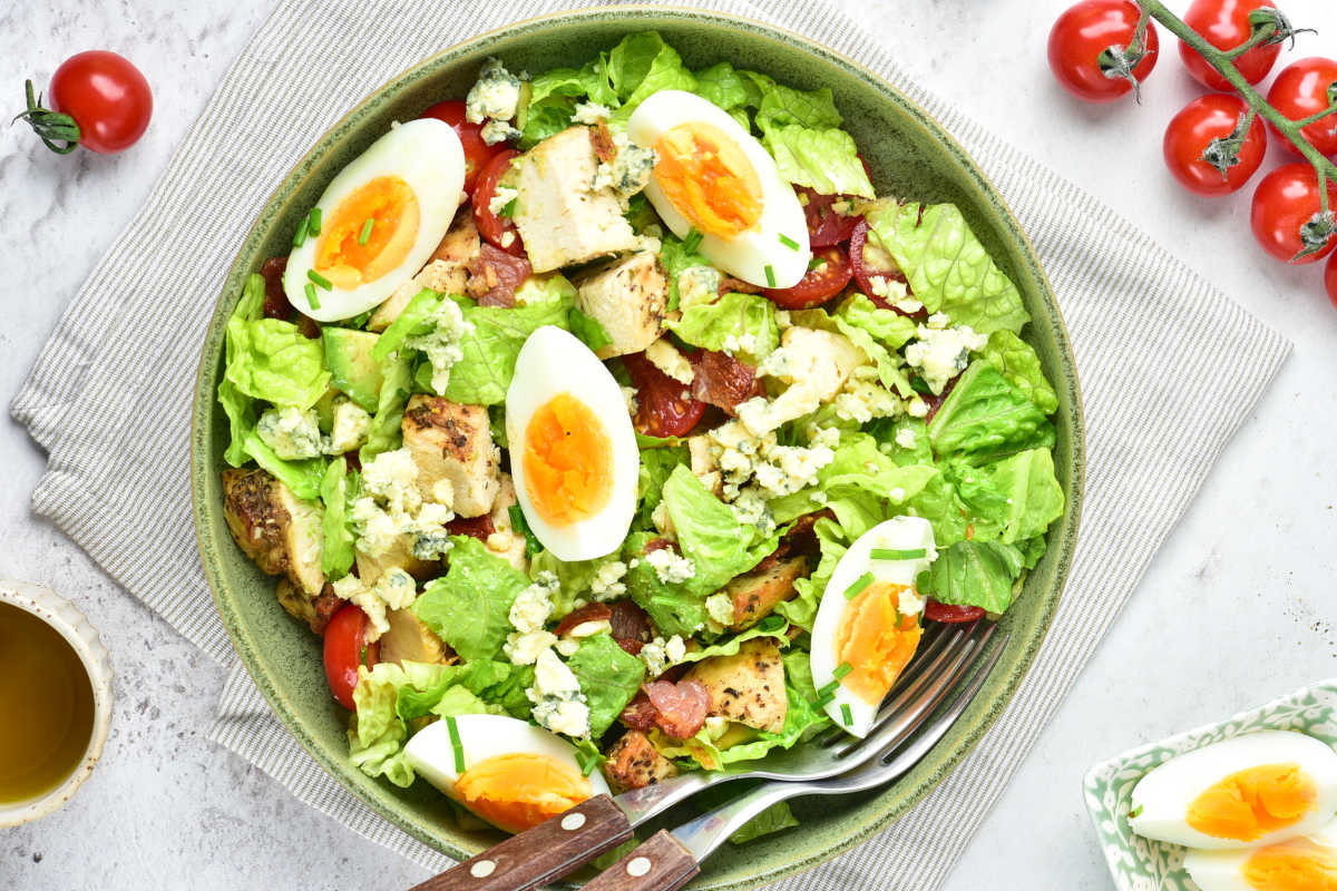 Bowl filled with cobb salad with romaine lettuce, medium boiled egg, blue cheese, and more in bowl ready to eat. 