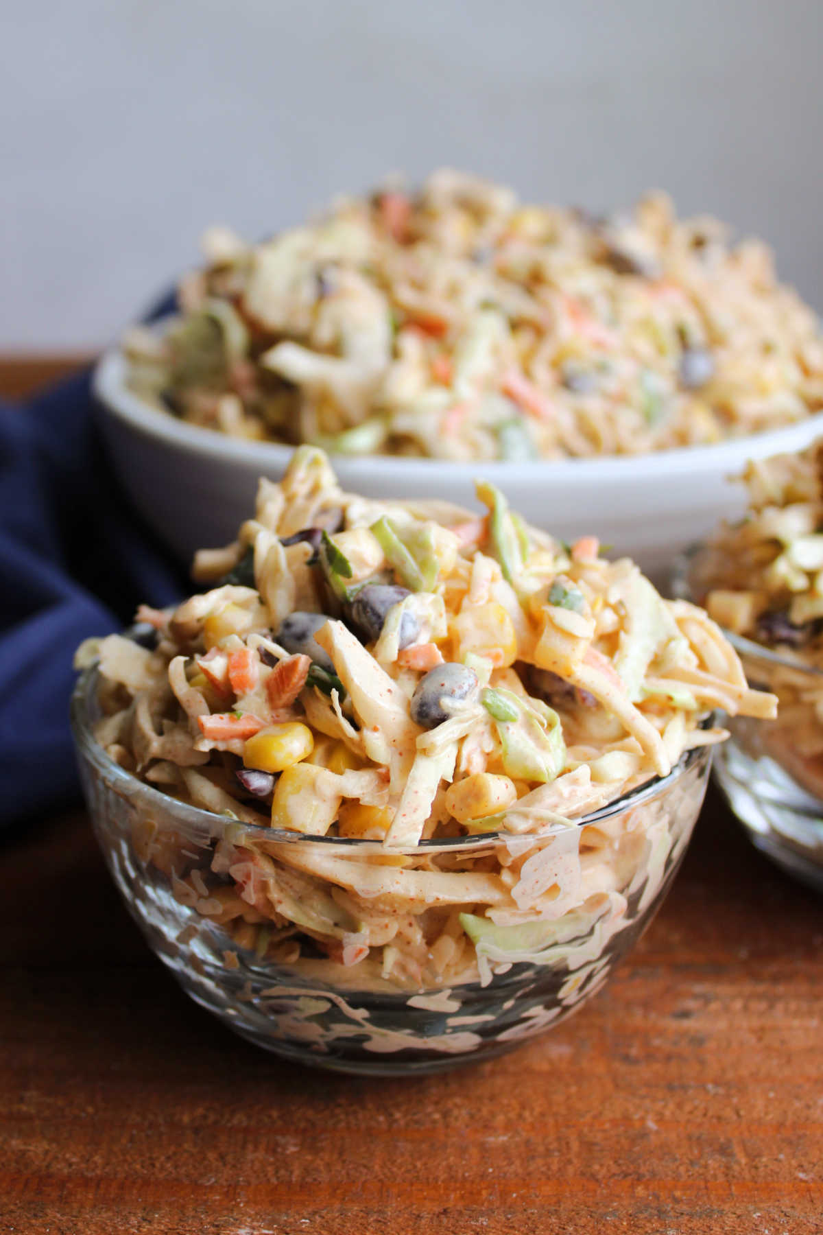 Two small glass bowls of southwestern coleslaw with corn, beans, cilantro and more, ready to be served and eaten. 