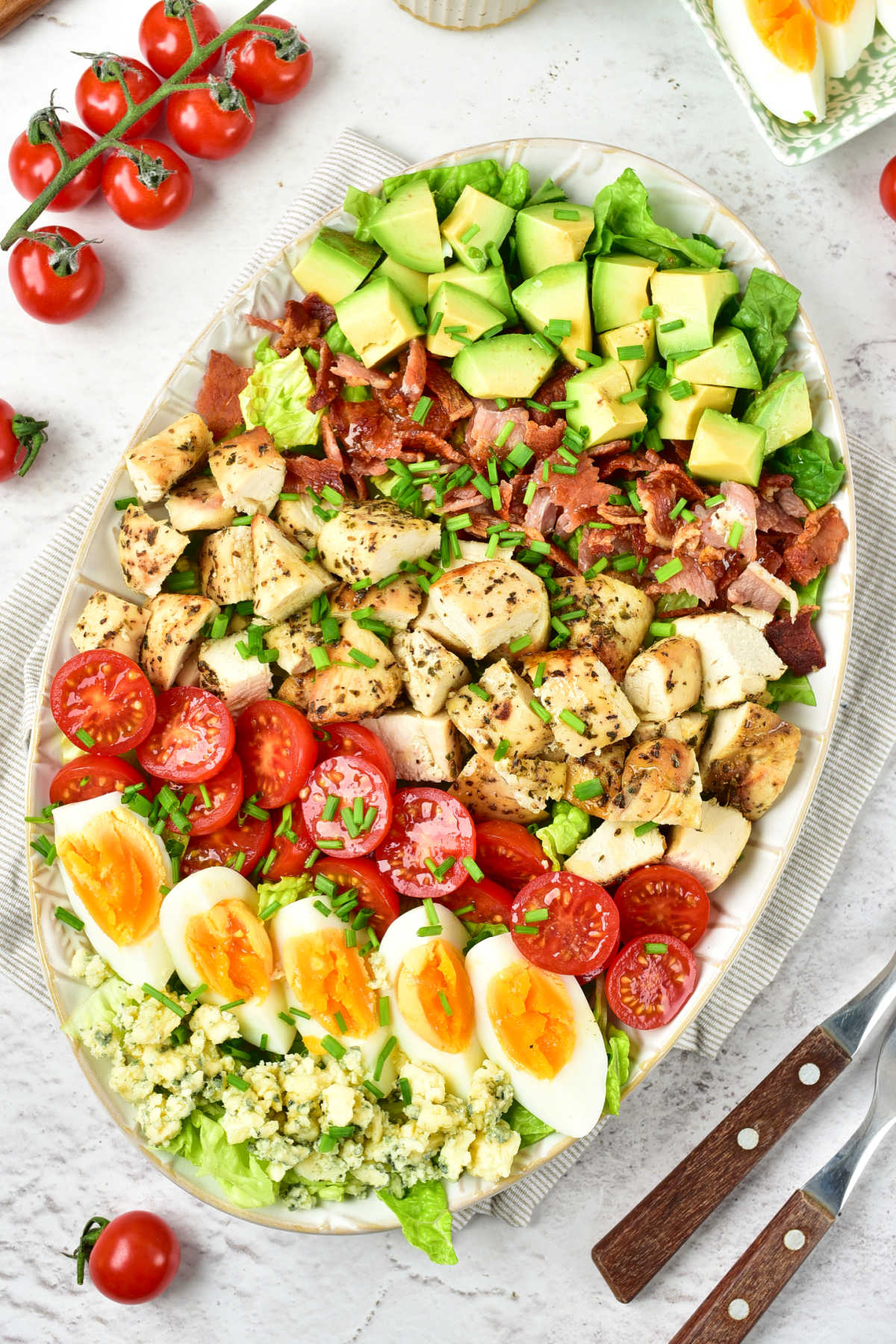 Serving platter filled with a homemade cobb salad with layers of savory toppings over a bed of lettuce. 