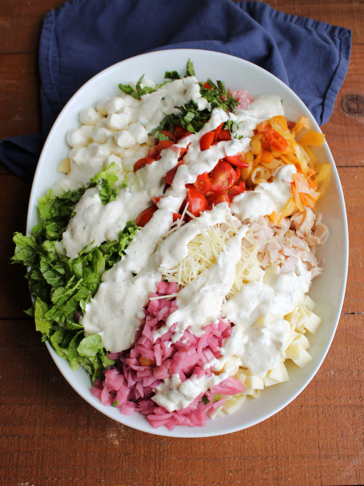 Grinder Pasta Salad 8 Dressing poured over bowl of Italian grinder pasta salad ingredients, ready to be tossed.
