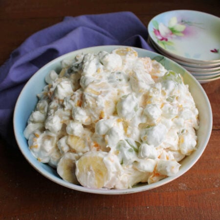Great Grandma's Grape Supreme Salad 1 Serving bowl filled with grape supreme salad with bananas, oranges, grapes, pineapple, and mini marshmallows in a creamy dressing.