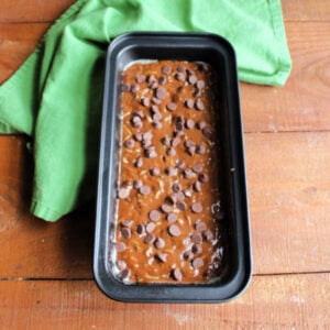 Loaf pan with chocolate zucchini bread batter topped with additional chocolate chips, ready to go in the oven.