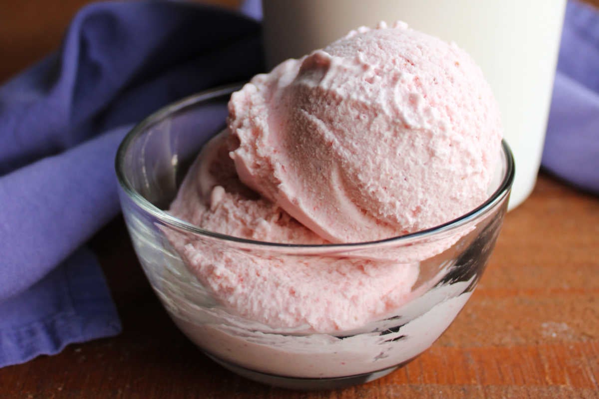 Homemade Strawberry Ice Cream Without Eggs 7 Close up of a small glass bowl filled with two scoops of homemade strawberry ice cream showing creamy texture and pretty pink hue.