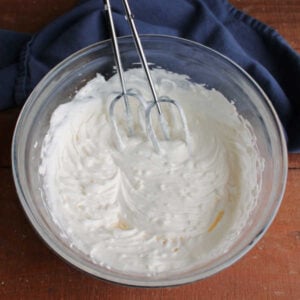 Mixing bowl filled with fluffy dressing for fruit salad made from dream whip and cream cheese with the beaters, ready for fruit.