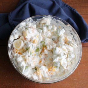 Mixing bowl filled with bananas, pineapple bits, oranges, grapes, and mini marshmallows in creamy dream whip and cream cheese dressing, ready to chill.