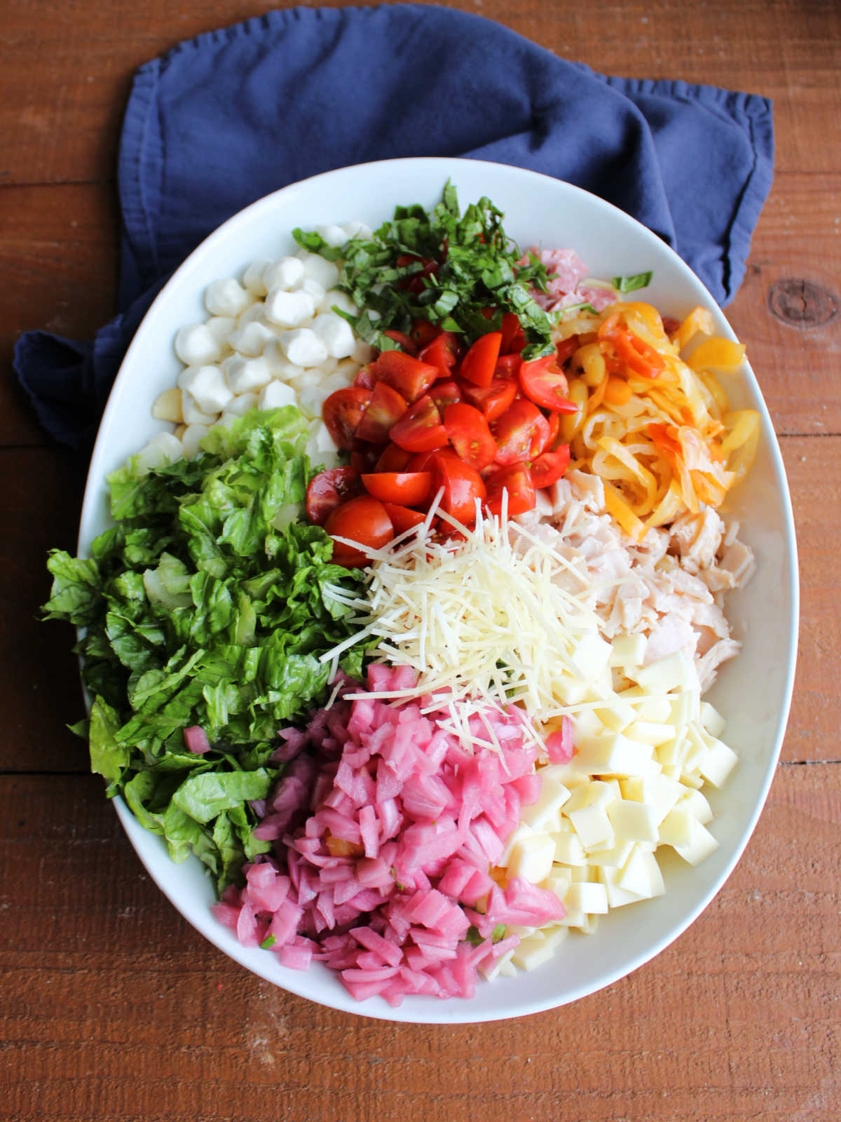 Grinder Pasta Salad 6 Large serving bowl filled with cooked pasta topped with mozzarella pearls, basil, tomatoes, pickled peppers, salami, turkey, provolone, pickled red onions. lettuce, and parmesan cheese, ready to dressing.
