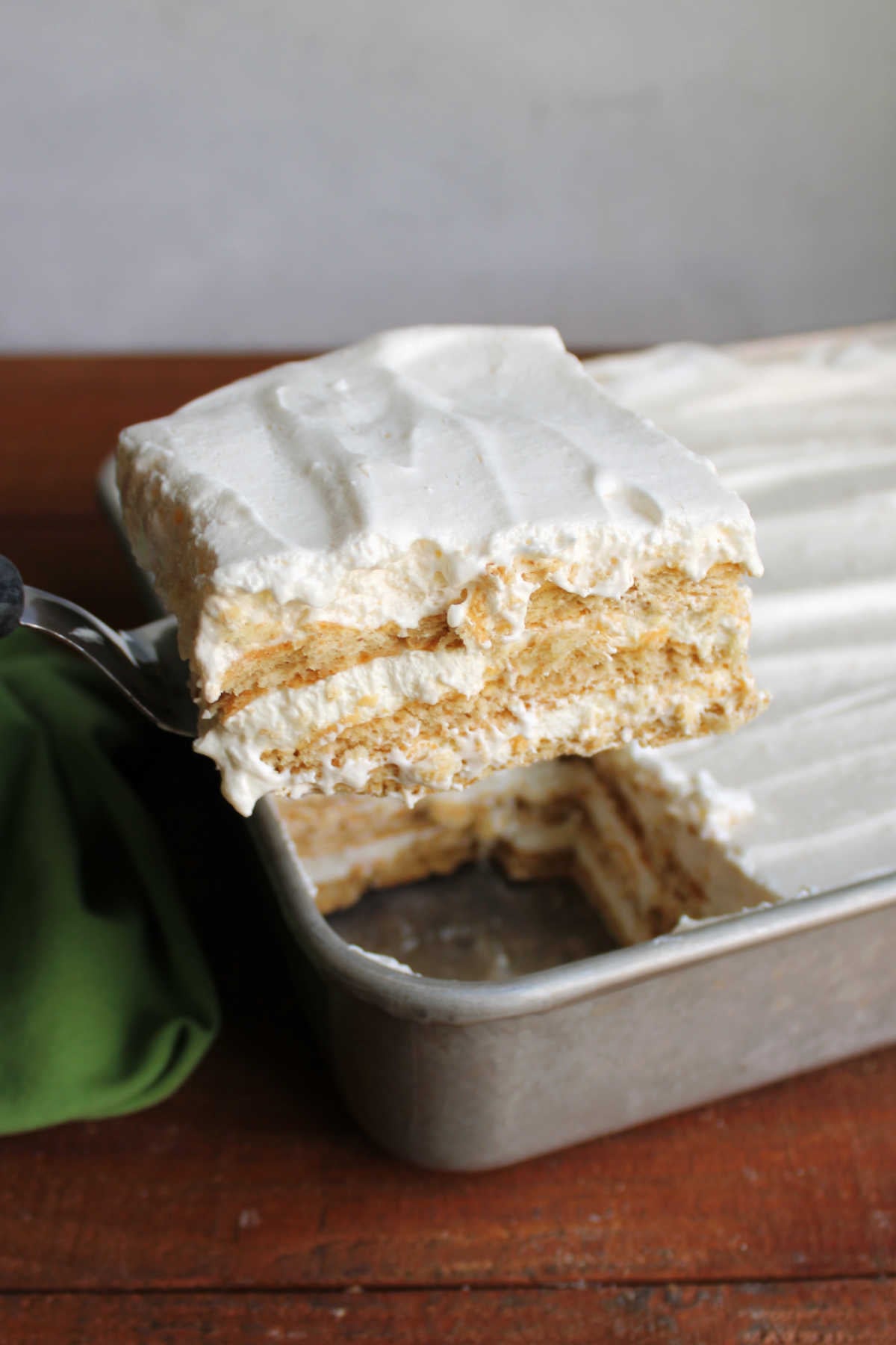 Spatula lifting piece of layered key lime icebox cake out of the pan. 