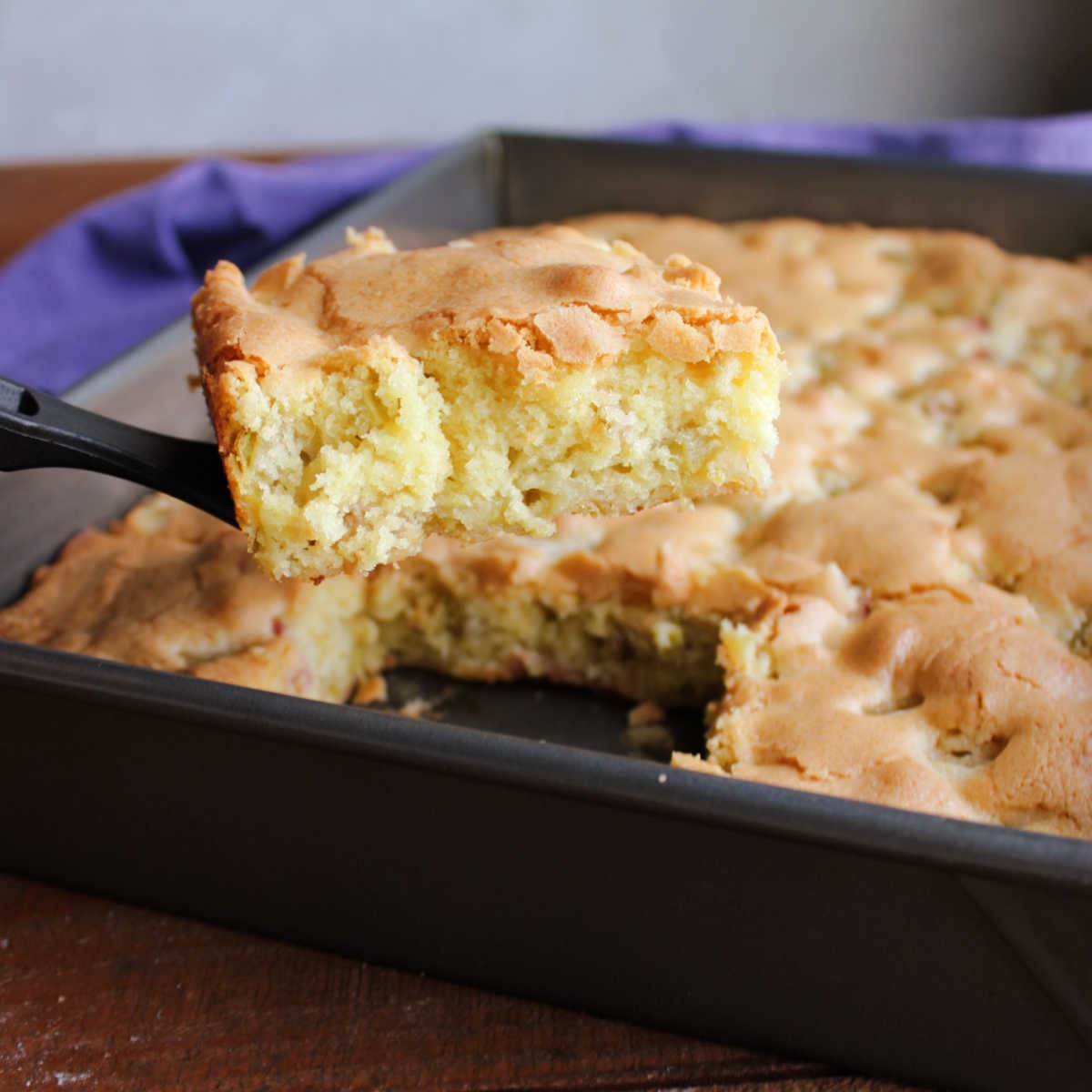 Rhubarb Snack Cake 5 Spatula lifting piece of rhubarb snack cake out of pan showing soft interior, golden crust, and bits of rhubarb throughout.