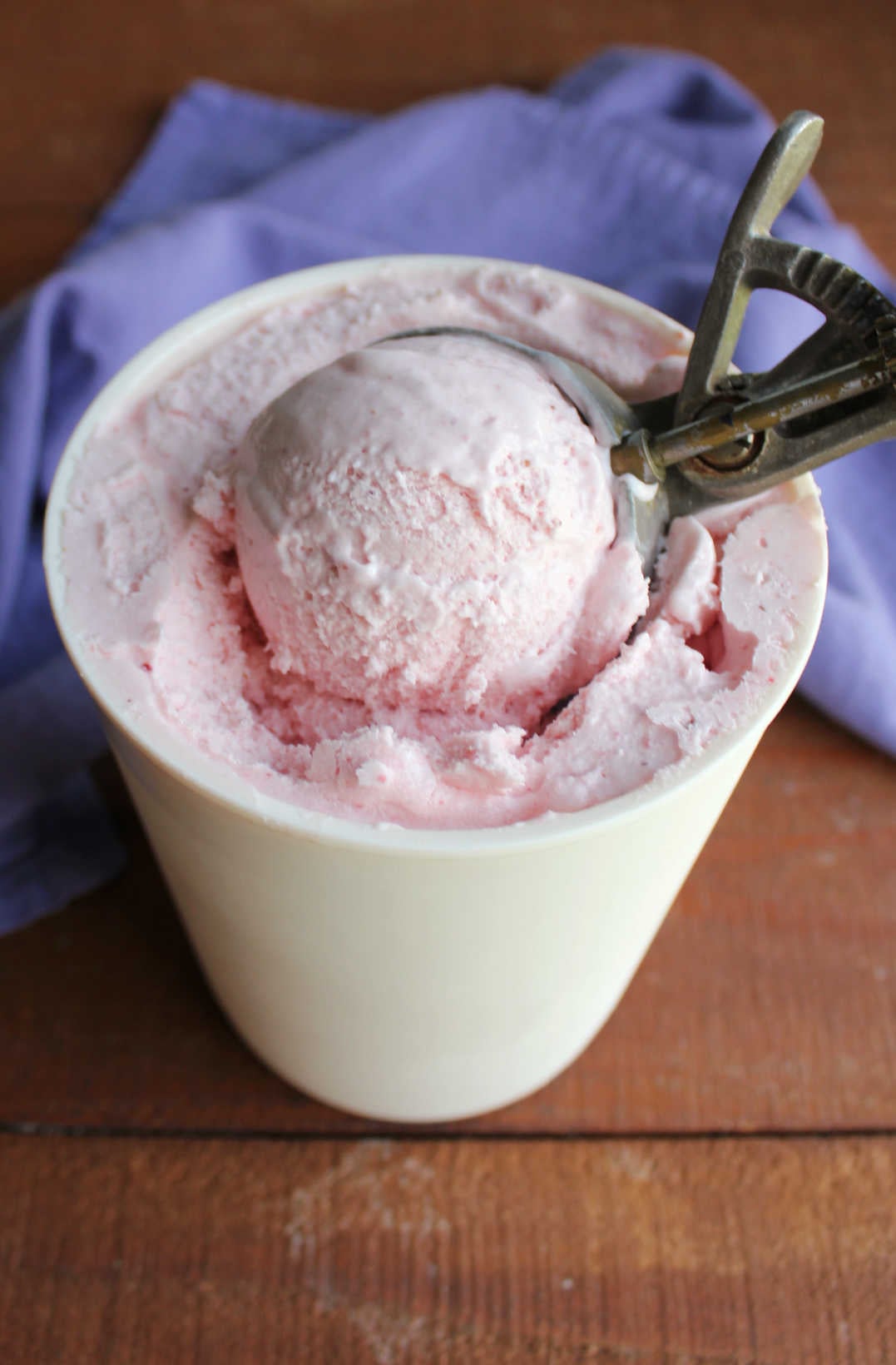 Homemade Strawberry Ice Cream Without Eggs 9 Ice cream scoop getting a ball of pink strawberry ice cream out of a freezer container.