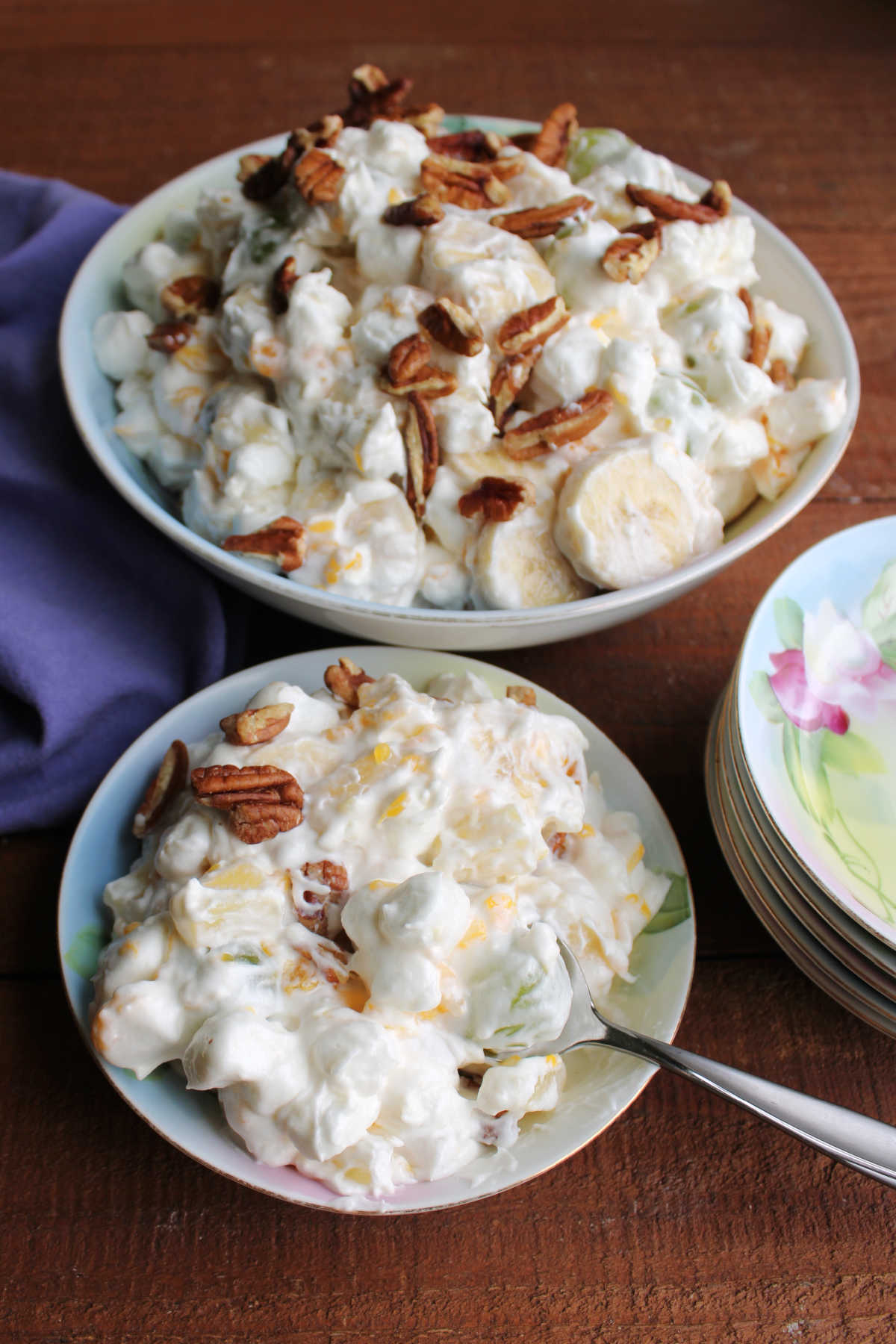 Small fruit bowl filled with grape supreme salad with various fruits and mini marshmallows in a creamy dressing topped with chopped pecans. 