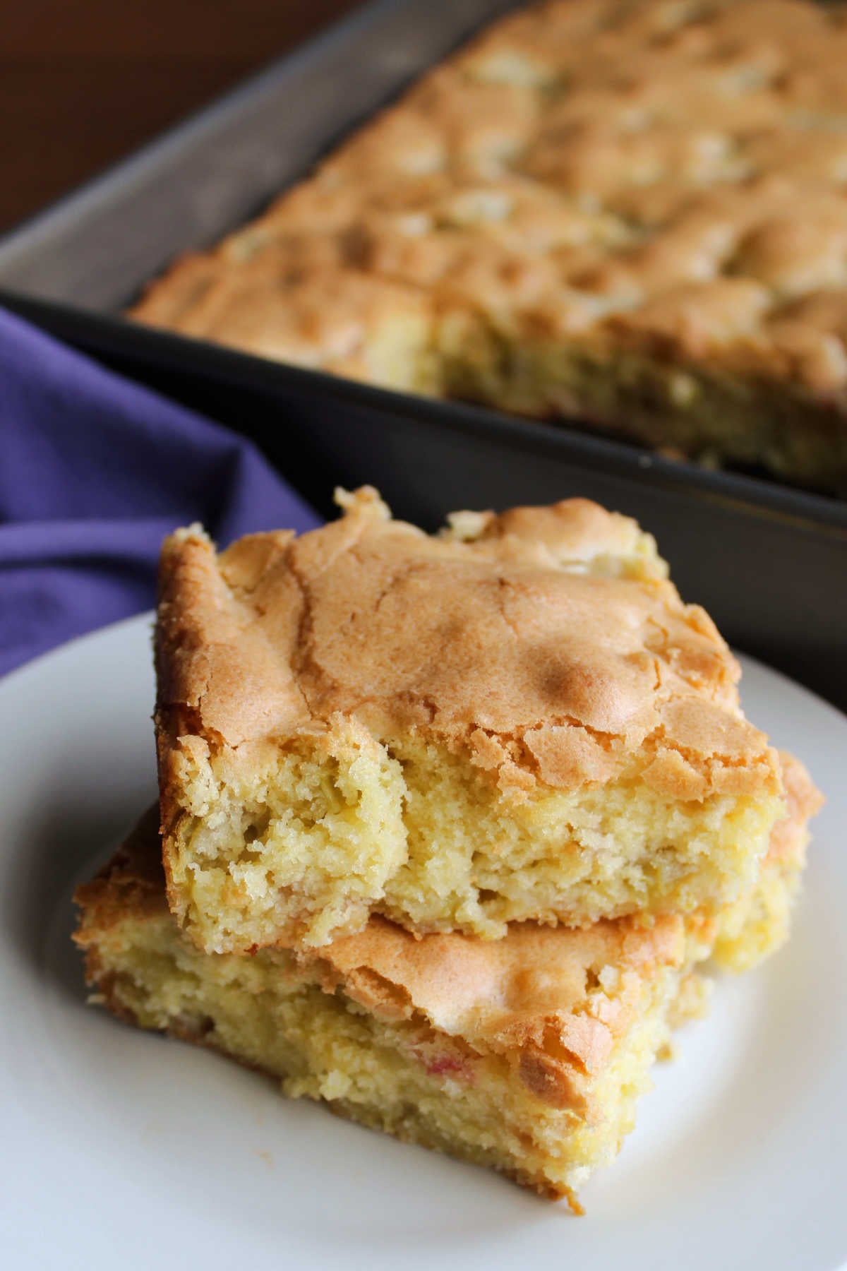 Rhubarb Snack Cake 8 Two pieces of tender rhubarb snack cake with a soft interior and golden exterior stacked on a small dessert plate.