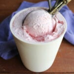 Ice cream scoop getting a ball of egg free strawberry ice cream out of a freezer container.