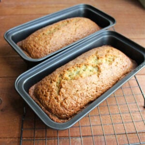 Two loaf pans with baked cucumber bread inside cooling on a wire rack.