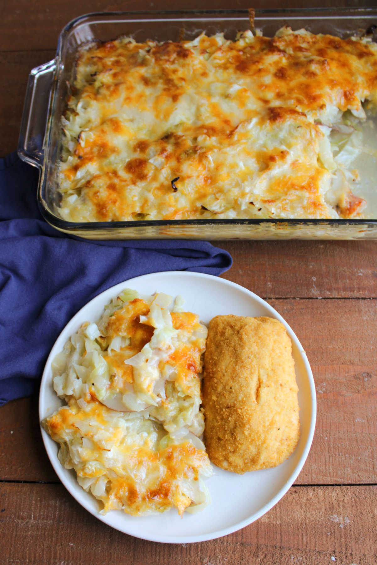 Dinner plate with a chicken cordon bleu served with a big helping of cabbage and potato casserole with the baking dish filled with the remaining casserole in the background. 
